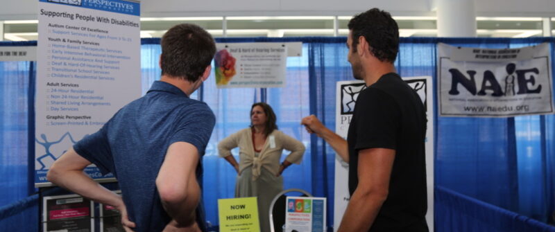 Two individuals using ASL at an exhibitor booth